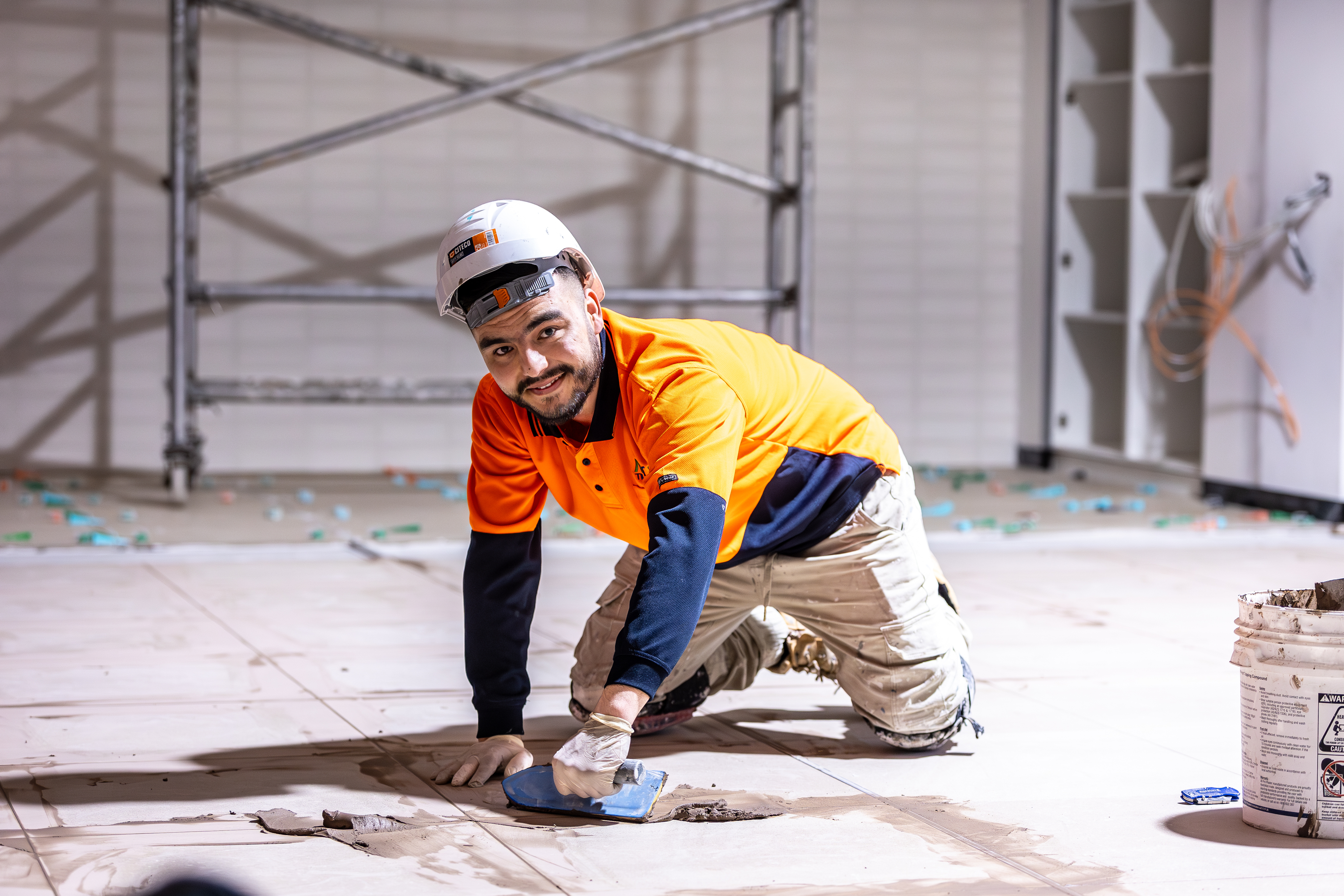 inside a commercial building grouting tiles grout High vis Employers Financial support for Employers tiler tiles young man laying tiles on a construction site blue-collar worker building clothing construction construction worker footwear ground hard hat helmet human face man person