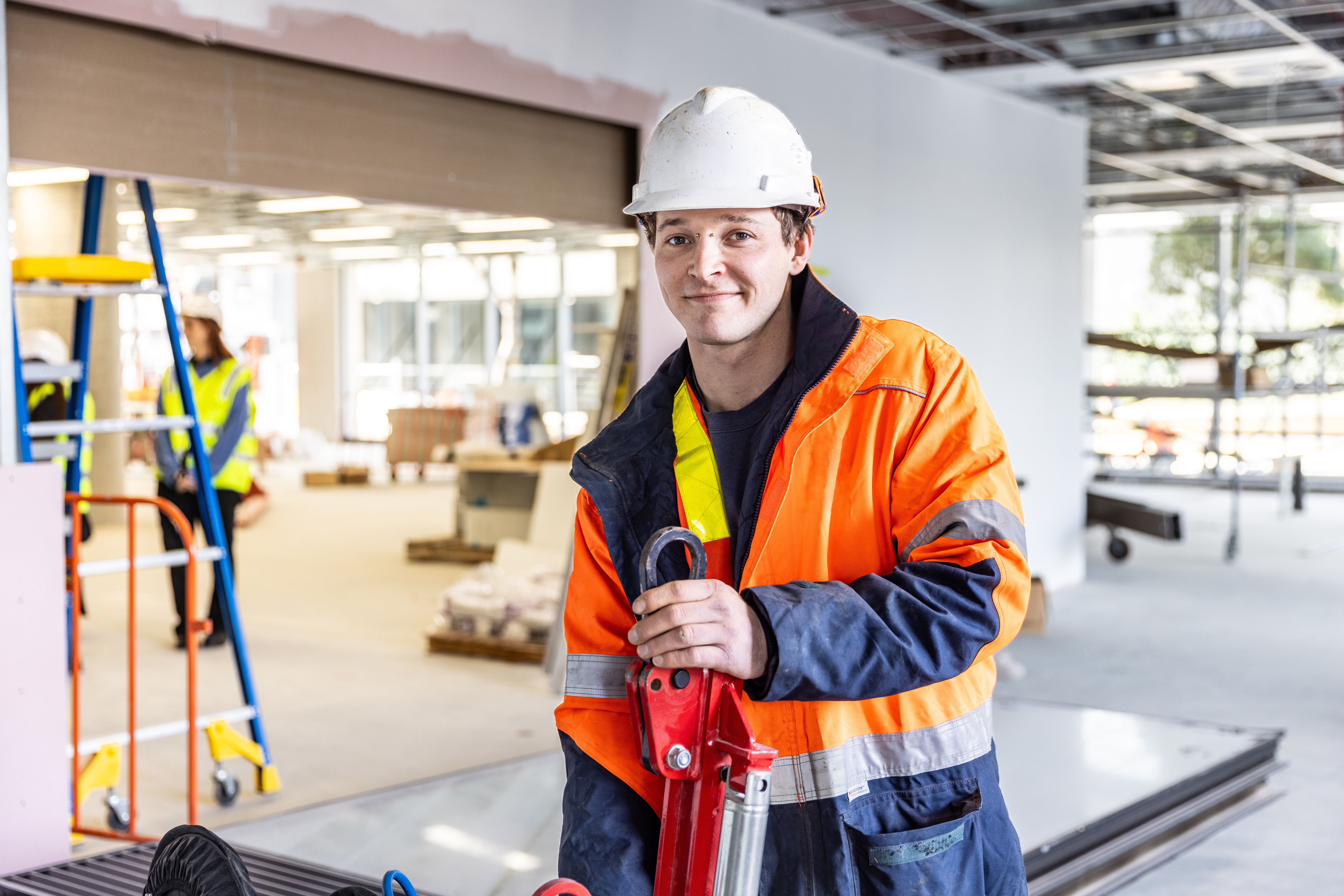 young man on construction site plastering in background construction site commercial site blue-collar worker building clothing construction construction worker engineer engineering hard hat helmet high-visibility clothing human face indoor man person workwear labour hire candidates high vi vest