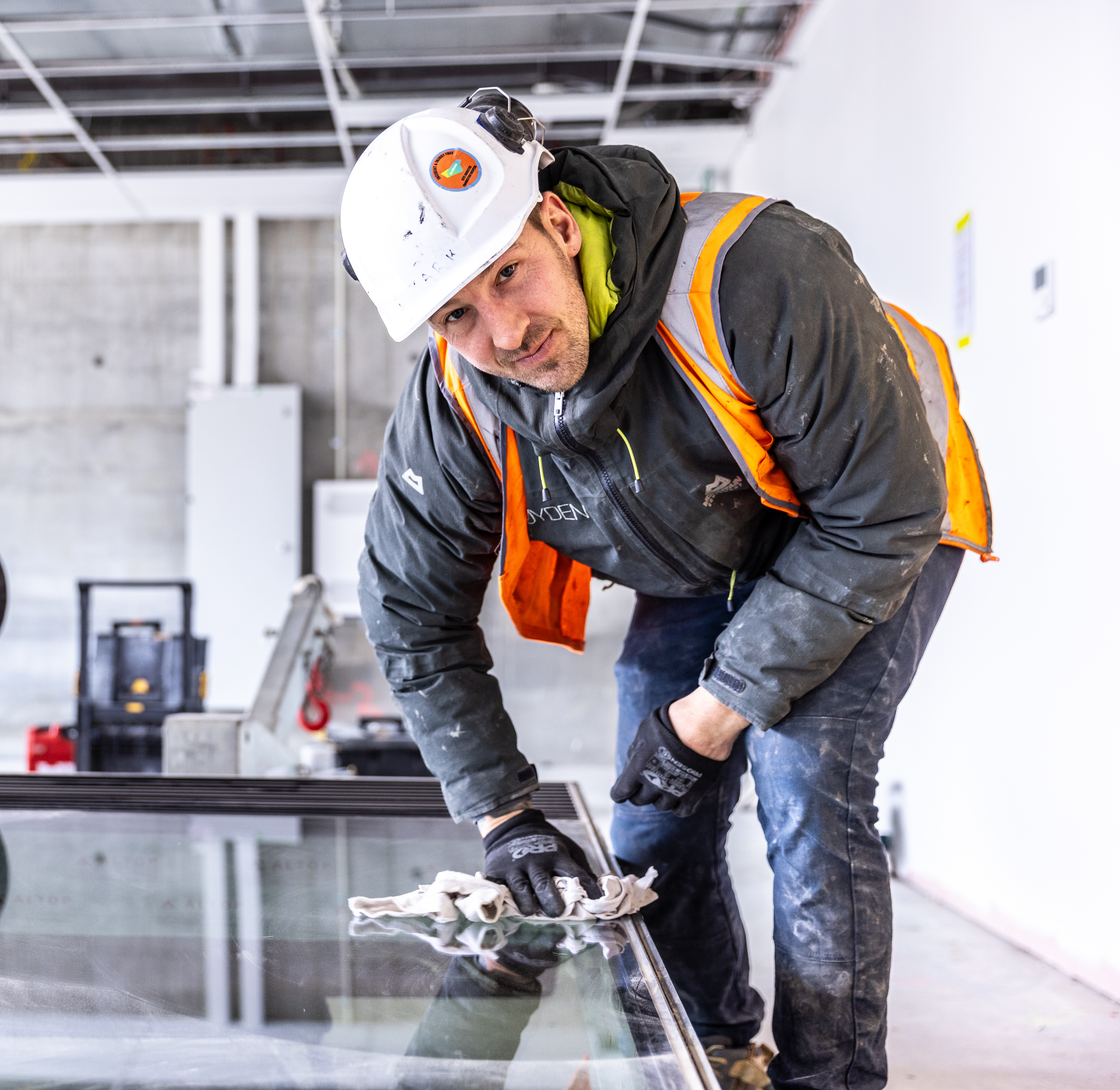 glazier window installation glass man cleaning window in preparation for installation construction site indoors commercial building protective gloves blue-collar worker clothing footwear indoor man person wall hardhat high vis vest window construction worker employers labour hire